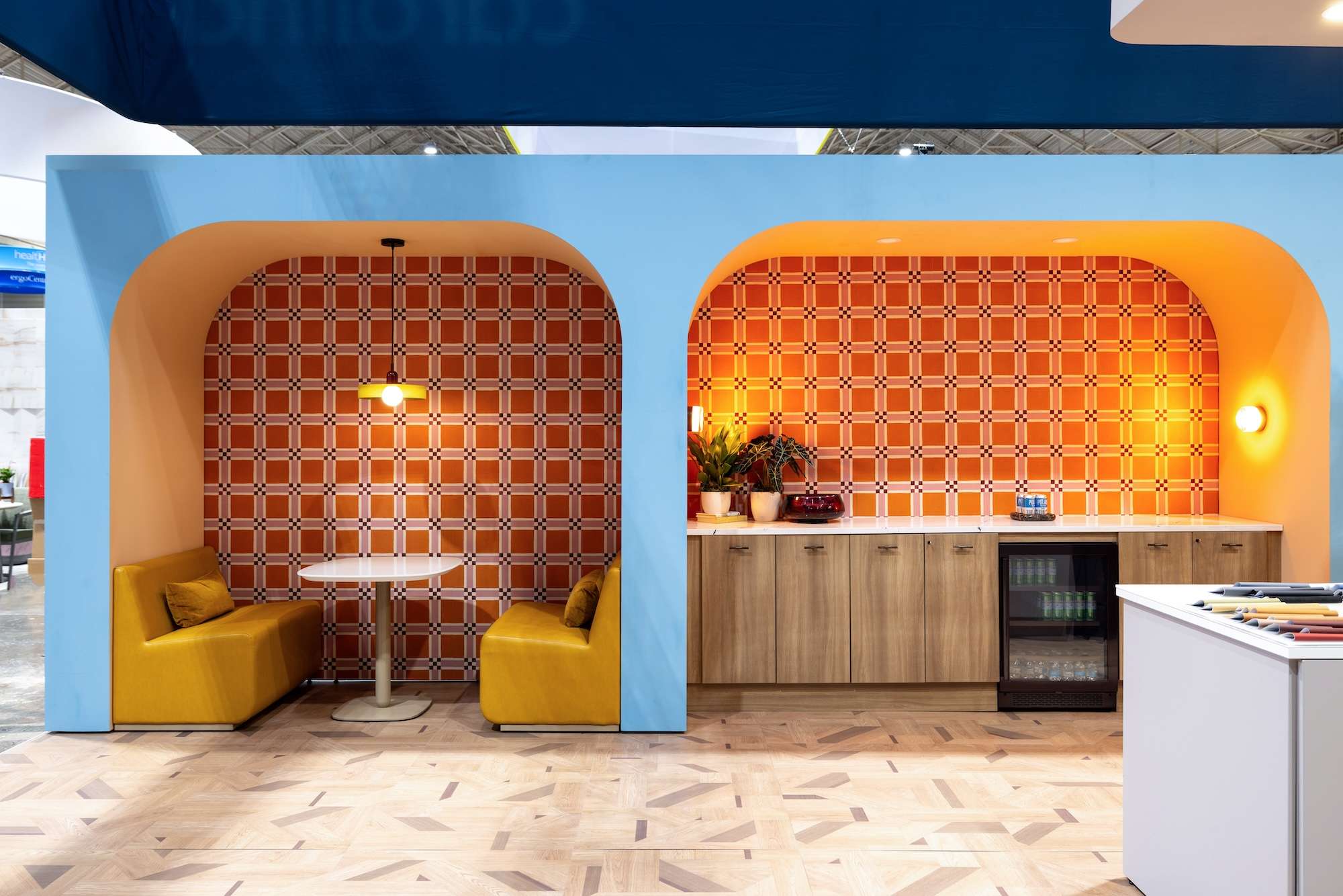 bright orange and yellow wallpaper with blue walls in arch frame over lounge modular Elara seating by Carolin with adjustable height table and cabinetry with fridge